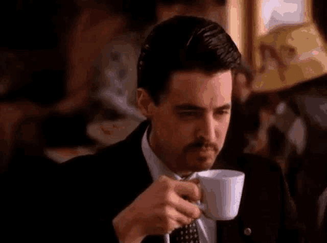 a man in a suit is drinking a cup of coffee .