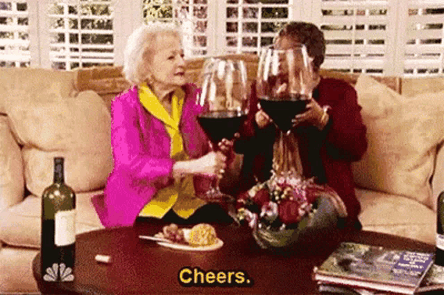 two older women are sitting on a couch holding glasses of wine .