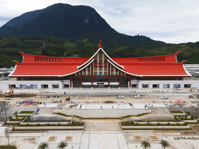 a large building with a red roof and a mountain in the background is under construction