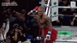 a man in a red skirt is standing in a boxing ring with a sign that says district in the background