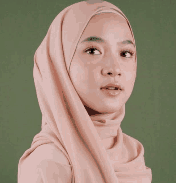 a woman wearing a pink hijab looks at the camera