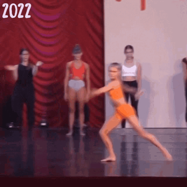 a girl in an orange outfit is dancing on a stage with the year 2022