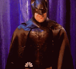 a man dressed as batman is standing in front of a purple curtain