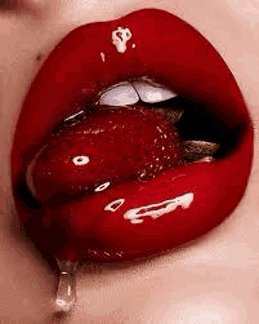 a close up of a woman 's lips with red lipstick and a strawberry sticking out of it .