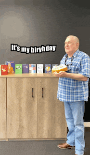 a man in a blue plaid shirt is holding a cake in front of a sign that says " it 's my birthday "