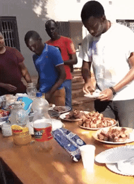 a group of men are gathered around a table with plates of food and a bottle of fanta on it