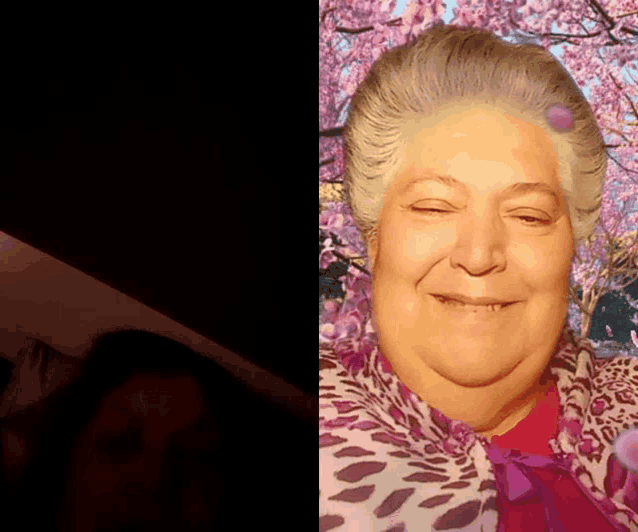 a woman with a purple flower on her head smiles in front of a cherry blossom tree