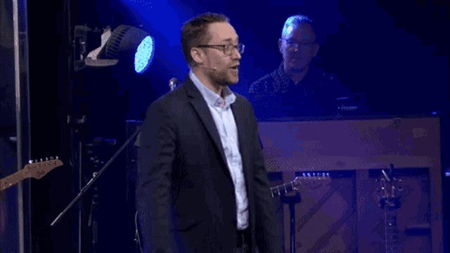 a man in a suit is dancing on a stage in front of a purple background
