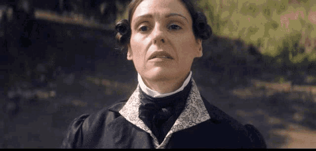 a woman in a black jacket and white collar is standing in front of a wall .