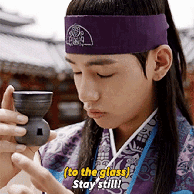 a young man wearing a purple headband is holding a cup and says " to the glass stay still "