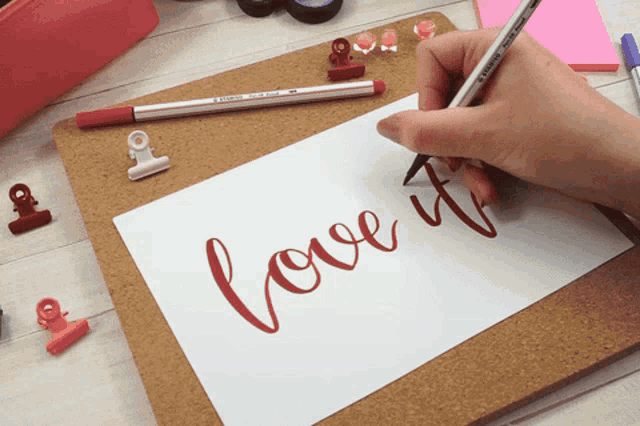 a person is writing the word love it in red on a piece of paper