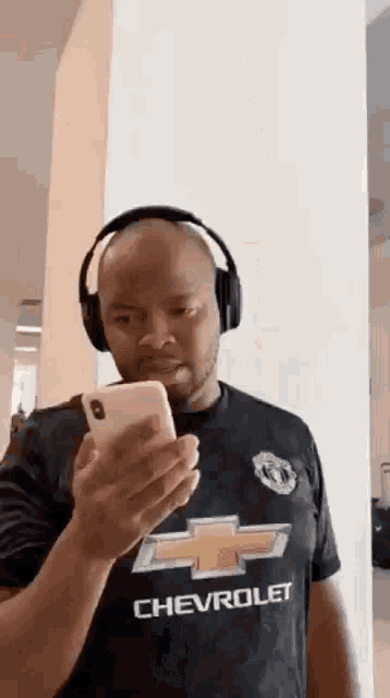 a man is wearing headphones and looking at his cell phone .