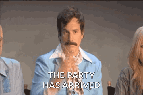 a man in a blue suit with a mustache is sitting at a table with other people .