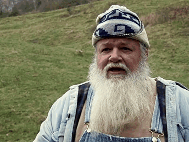 a man with a beard wearing overalls and a hat with the letter t on it