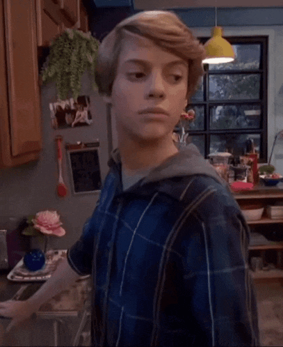 a young boy is standing in a kitchen looking at the camera .