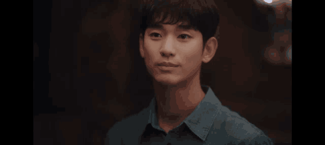 a young man in a blue shirt is looking at the camera and smiling .
