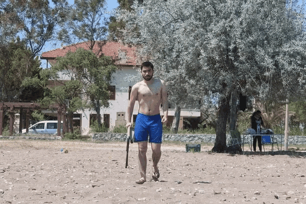 a shirtless man in blue shorts walking on a sandy beach