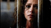 a woman is behind bars in a jail cell with a sad look on her face .