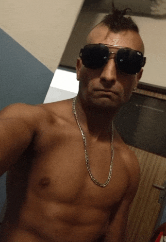 a shirtless man wearing sunglasses and a chain takes a selfie