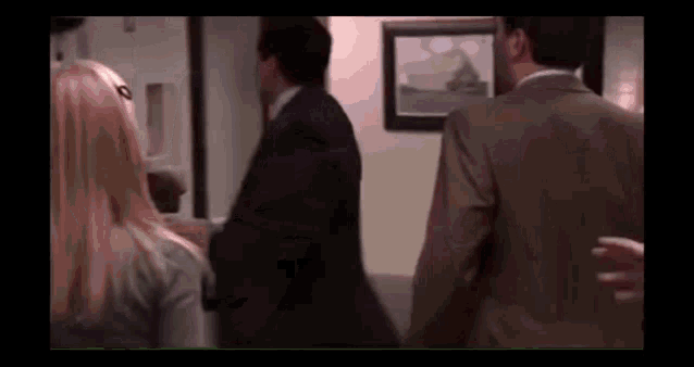 a man in a suit and a woman in a sweater are walking in a room