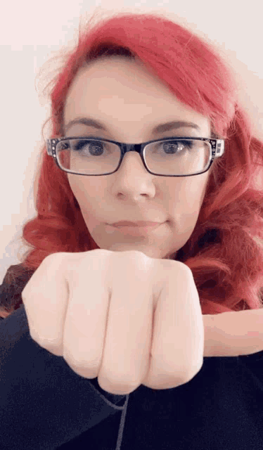 a woman with red hair and glasses holds her fist up in the air