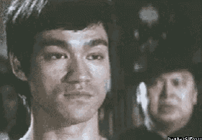 bruce lee is looking at the camera while a man in a police hat stands behind him .