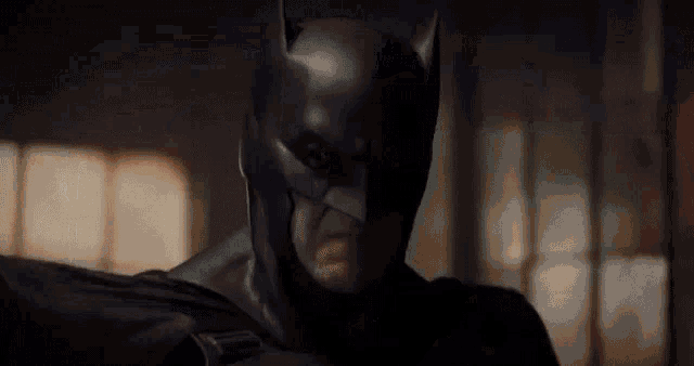 a man in a batman costume is holding a gun in his hand .