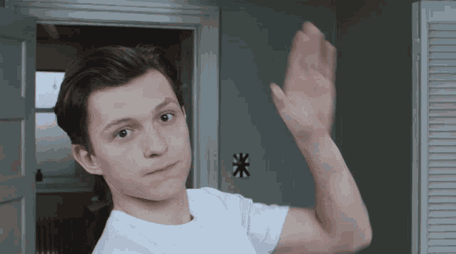 a young man in a white shirt waves his hand in front of a door