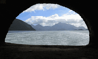 a view of a body of water with mountains in the background is shown through a hole in a rock