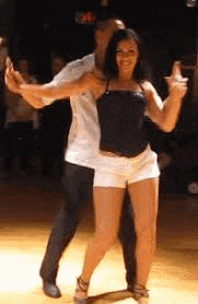 a man and a woman are dancing on a dance floor . the woman is wearing shorts and a black top .