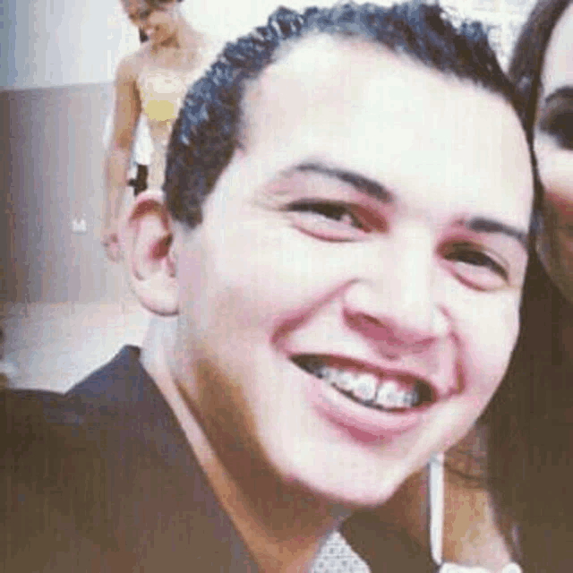 a young man with braces on his teeth is smiling for the camera while standing next to a woman .