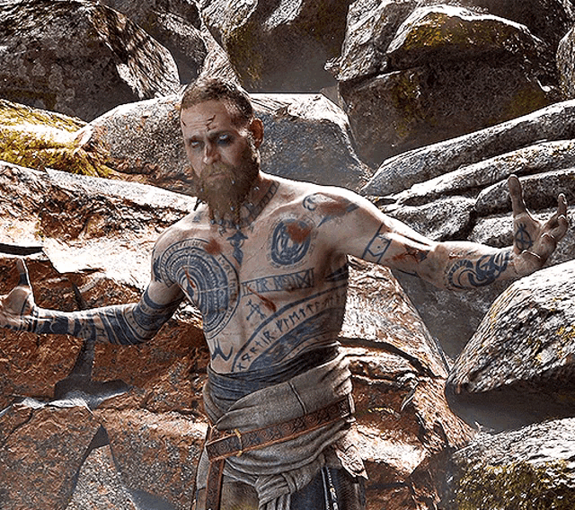 a man with a beard and tattoos on his torso is standing in front of a pile of rocks with his arms outstretched