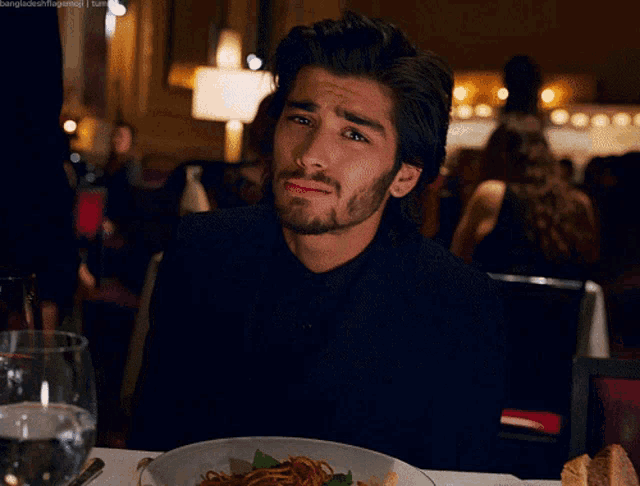 a man in a black shirt sits at a table with a plate of food and a glass of water