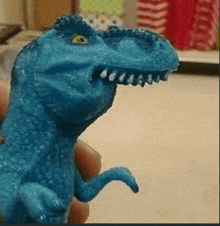 a person is holding a blue toy dinosaur with a large mouth