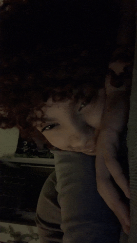 a woman with curly hair is laying down with her hand on her chin