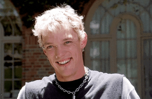 a young man with piercings and a chain around his neck smiles at the camera