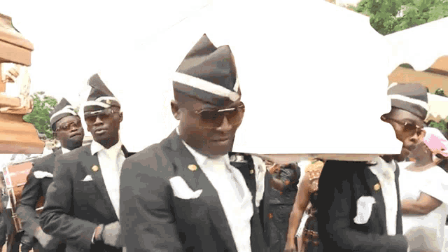 a group of men in black suits are carrying a coffin