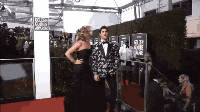 a man in a tuxedo and a woman in a black dress are on the red carpet at the golden globe awards