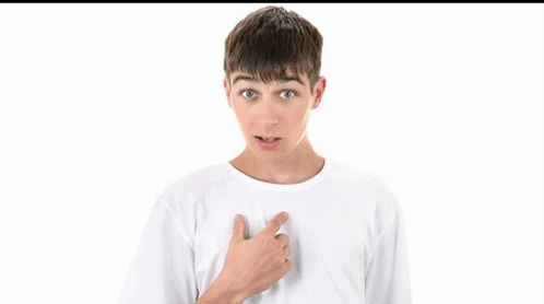 a young boy in a white t-shirt is pointing at his chest .