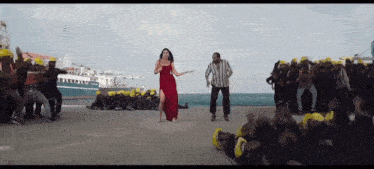 a woman in a red dress is dancing in front of a crowd of people wearing hard hats