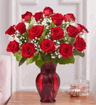 a vase filled with red roses and baby 's breath is sitting on a wooden table .