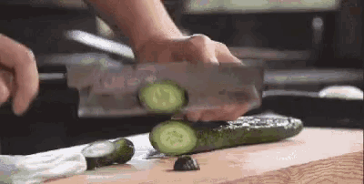 a person is cutting a cucumber with a large knife on a cutting board .
