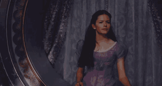 a woman in a purple dress is looking in a mirror