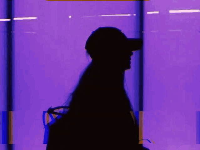 a silhouette of a woman wearing a hat and headphones is walking in front of a purple wall .