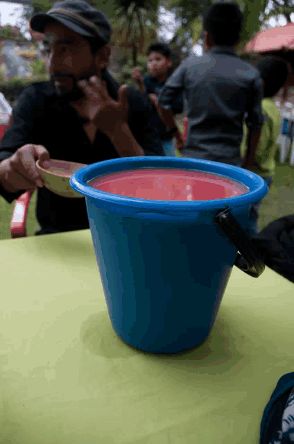 a blue bucket filled with red liquid sits on a table next to a man