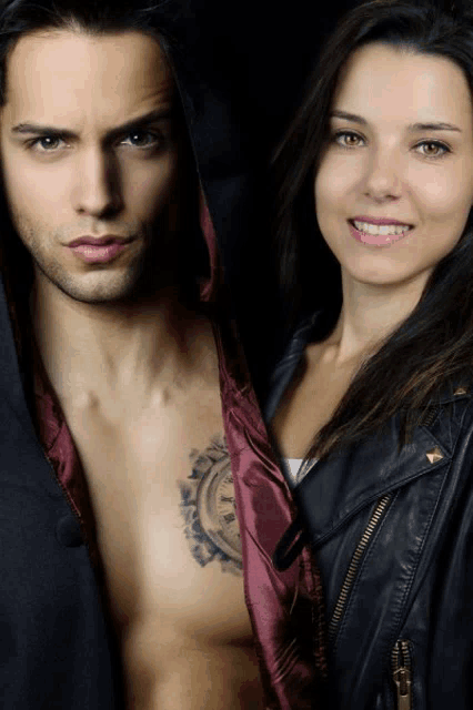 a man with a tattoo on his chest stands next to a woman in a leather jacket