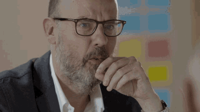 a man with glasses and a beard holds his hand to his mouth