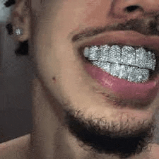 a close up of a man 's mouth with a beard and grills on his teeth .