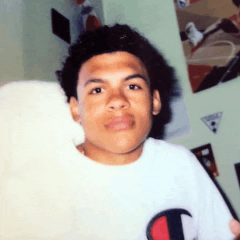 a young man with curly hair is wearing a white t-shirt and looking at the camera .