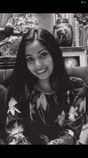 a black and white photo of a smiling woman with a vase in the background